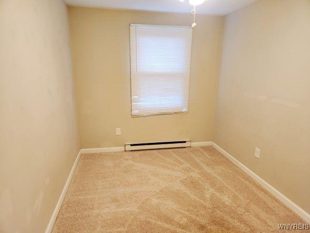 unfurnished room featuring carpet floors and a baseboard heating unit