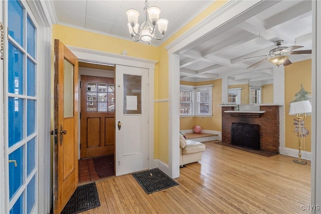 foyer entrance featuring coffered ceiling, light hardwood / wood-style flooring, a brick fireplace, ceiling fan with notable chandelier, and beamed ceiling