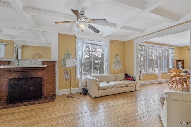 living room with a fireplace, light wood-type flooring, ceiling fan, coffered ceiling, and beam ceiling