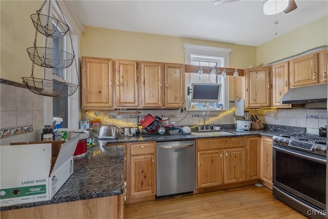 kitchen featuring light wood-type flooring, dark stone counters, appliances with stainless steel finishes, ceiling fan, and sink