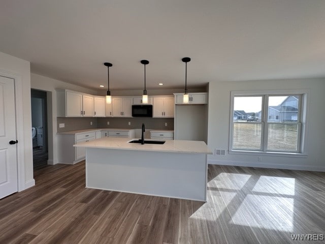 kitchen featuring white cabinets, a center island with sink, hanging light fixtures, dark hardwood / wood-style flooring, and sink