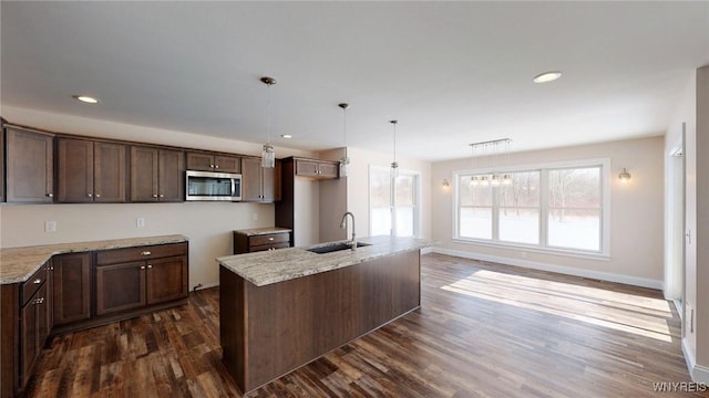 kitchen featuring an island with sink, light stone countertops, pendant lighting, dark wood-type flooring, and sink