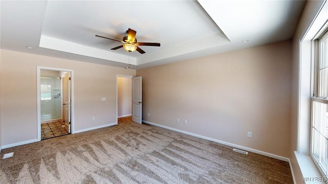 unfurnished bedroom with a raised ceiling, light carpet, ceiling fan, and ensuite bath