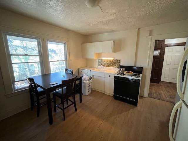 kitchen featuring gas range, a textured ceiling, dark hardwood / wood-style floors, white fridge, and white cabinets