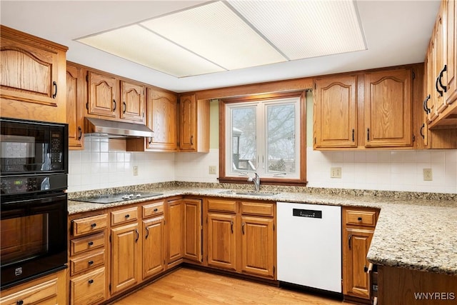 kitchen featuring black appliances, tasteful backsplash, sink, light wood-type flooring, and light stone counters