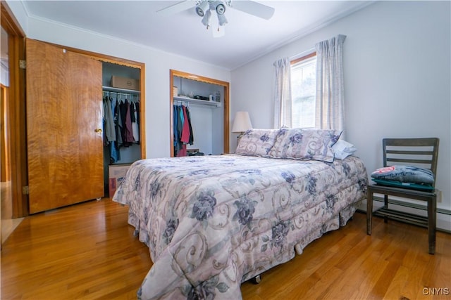 bedroom featuring a baseboard heating unit, light wood-type flooring, ceiling fan, and multiple closets