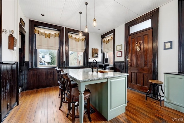 kitchen with sink, a kitchen breakfast bar, pendant lighting, light stone countertops, and a kitchen island with sink