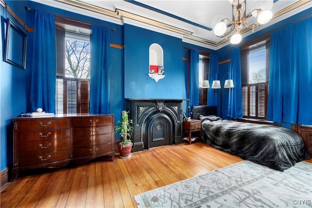 bedroom featuring a fireplace, an inviting chandelier, hardwood / wood-style flooring, and crown molding