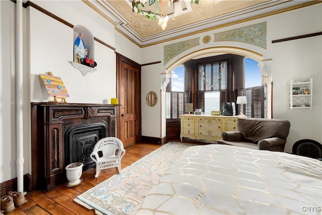 bedroom featuring multiple windows, hardwood / wood-style floors, a wood stove, and crown molding