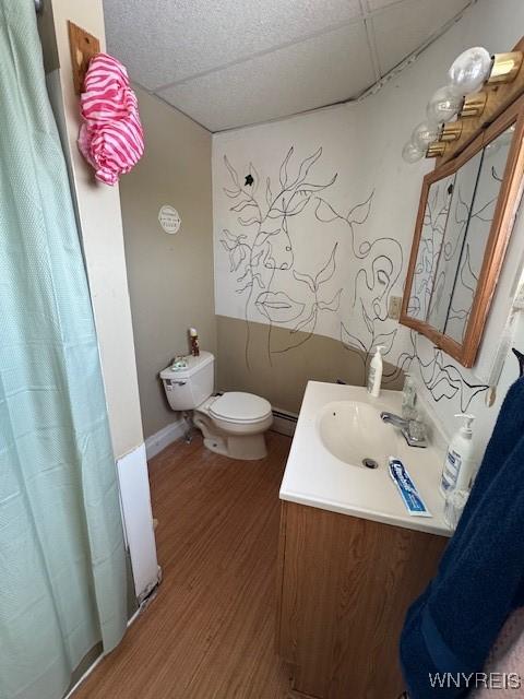 bathroom featuring hardwood / wood-style flooring, a paneled ceiling, toilet, vanity, and baseboard heating