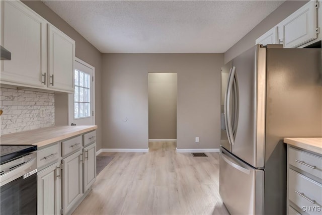 kitchen with a textured ceiling, stainless steel appliances, decorative backsplash, light wood-type flooring, and white cabinetry