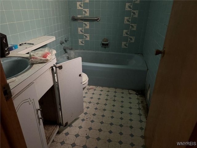 bathroom with toilet, a tub, tile walls, and vanity