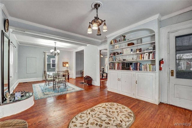 living area featuring built in shelves, an inviting chandelier, crown molding, and hardwood / wood-style flooring