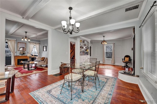 dining room featuring beamed ceiling, ornamental molding, hardwood / wood-style flooring, a chandelier, and built in shelves