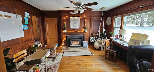 living area with ceiling fan, light hardwood / wood-style flooring, wooden walls, and a wood stove