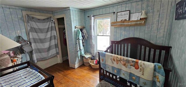 bedroom featuring hardwood / wood-style floors, wooden walls, and a crib