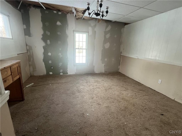 basement featuring a notable chandelier, a paneled ceiling, and carpet