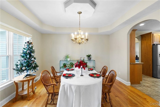 dining space with light hardwood / wood-style floors, a healthy amount of sunlight, a tray ceiling, and a notable chandelier