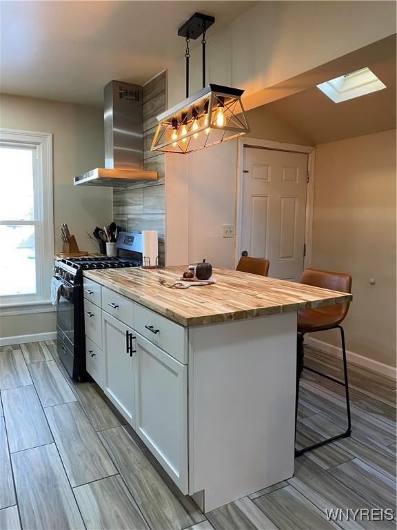 kitchen featuring a kitchen breakfast bar, range with gas stovetop, butcher block countertops, white cabinetry, and range hood