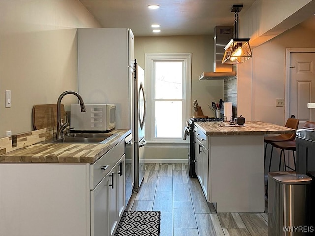 kitchen with stainless steel appliances, sink, decorative light fixtures, butcher block countertops, and wall chimney range hood