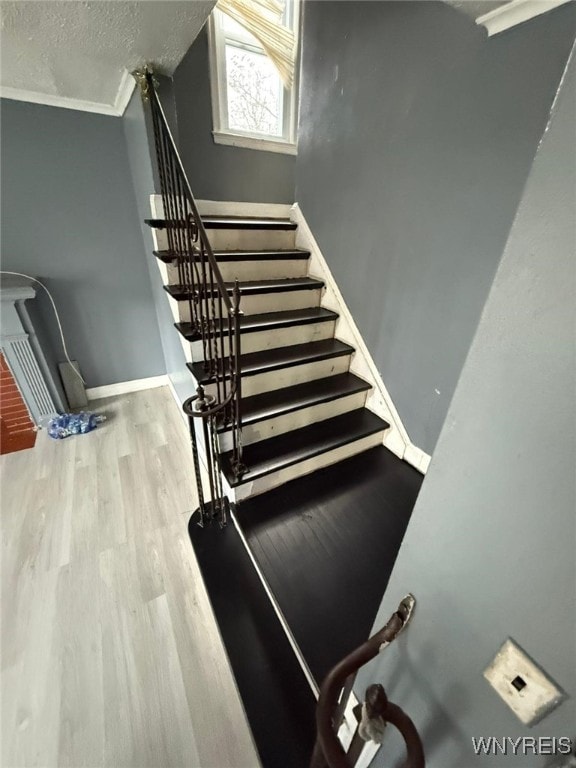 stairs with a textured ceiling, crown molding, and hardwood / wood-style flooring