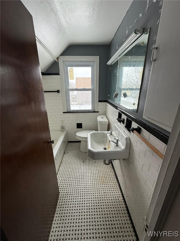 bathroom featuring sink, a textured ceiling, lofted ceiling, tile walls, and a bathing tub