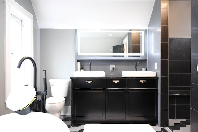 bathroom with tile walls, toilet, vaulted ceiling, and vanity