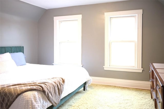 bedroom with light colored carpet, vaulted ceiling, and multiple windows