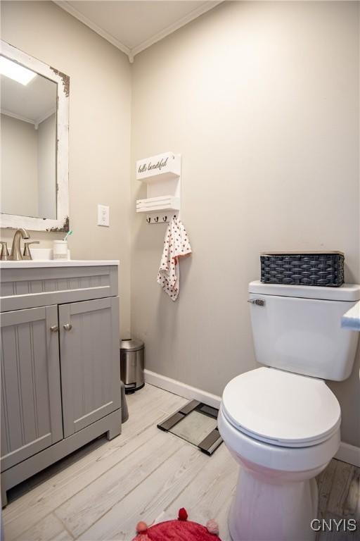 bathroom with toilet, wood-type flooring, vanity, and ornamental molding