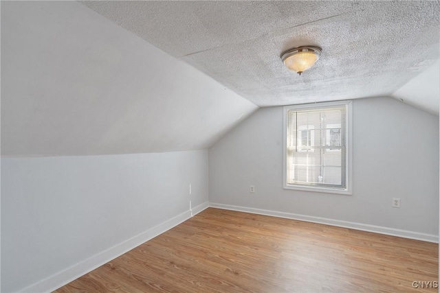 additional living space featuring lofted ceiling, a textured ceiling, and light hardwood / wood-style flooring