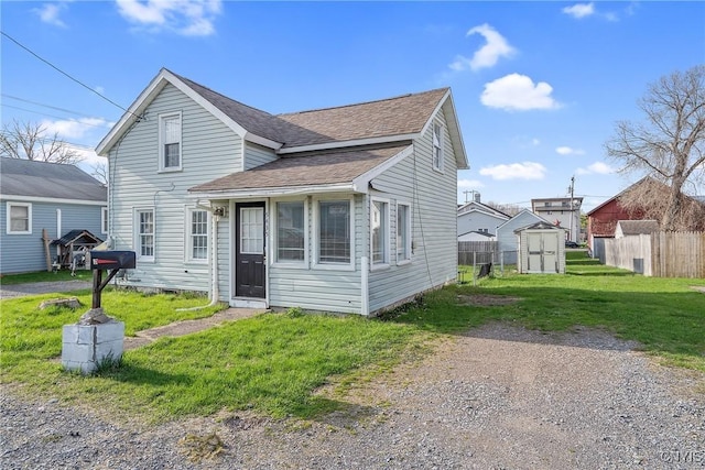 view of front of property featuring a storage shed, roof with shingles, a front yard, and fence