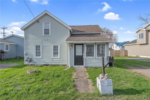 traditional home with a front yard, a shingled roof, and fence