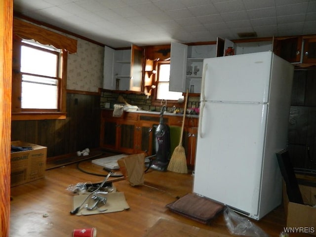 kitchen featuring white fridge, a wealth of natural light, light hardwood / wood-style floors, and wooden walls