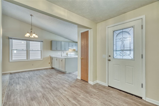 entryway with vaulted ceiling, light wood-type flooring, a notable chandelier, and a wealth of natural light