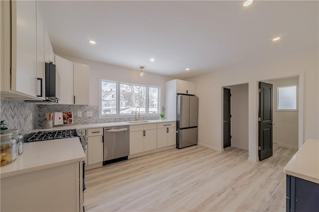 kitchen featuring stainless steel appliances, sink, white cabinets, tasteful backsplash, and light hardwood / wood-style flooring