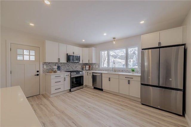 kitchen with white cabinets, stainless steel appliances, sink, light hardwood / wood-style flooring, and backsplash