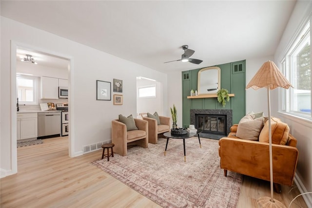 living room with a fireplace, ceiling fan, light hardwood / wood-style floors, and plenty of natural light