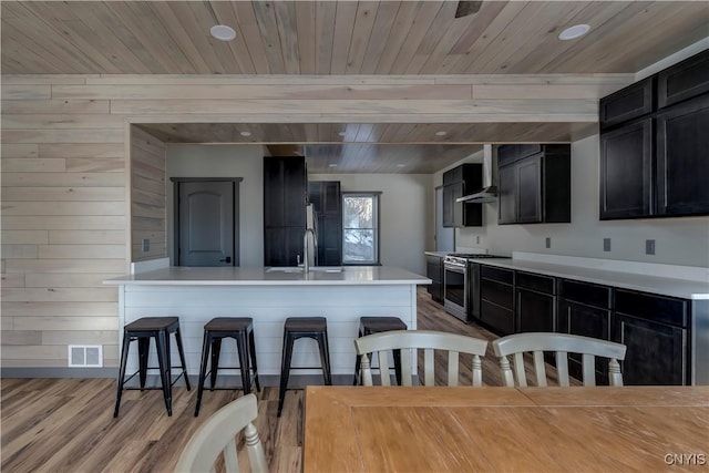 kitchen with sink, wooden ceiling, stainless steel gas range, a breakfast bar area, and wood walls