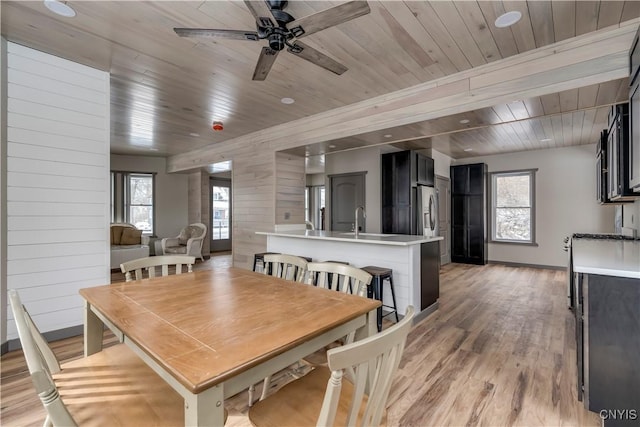 dining area with ceiling fan, light hardwood / wood-style flooring, wooden walls, and sink