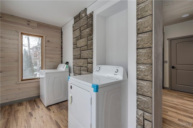 laundry area featuring separate washer and dryer, light wood-type flooring, and wooden walls