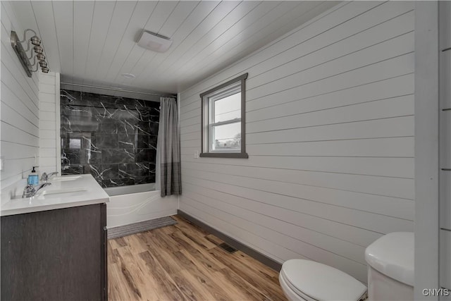 full bathroom featuring wooden walls, hardwood / wood-style floors, toilet, shower / bathing tub combination, and vanity