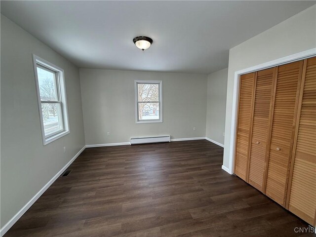 unfurnished bedroom featuring a closet, a baseboard radiator, dark hardwood / wood-style flooring, and multiple windows