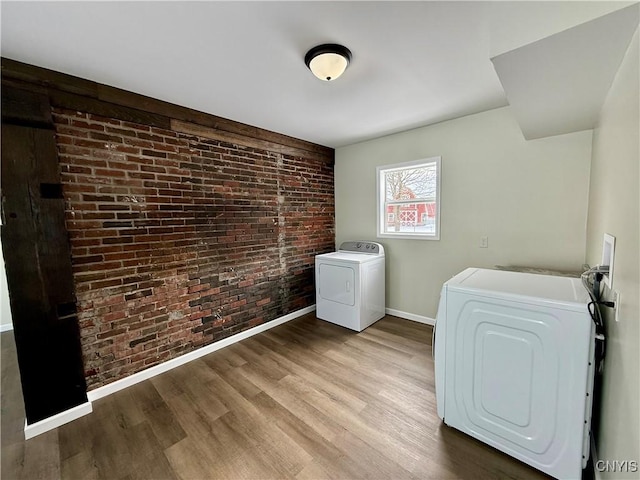 laundry room featuring brick wall, washing machine and dryer, and light hardwood / wood-style flooring