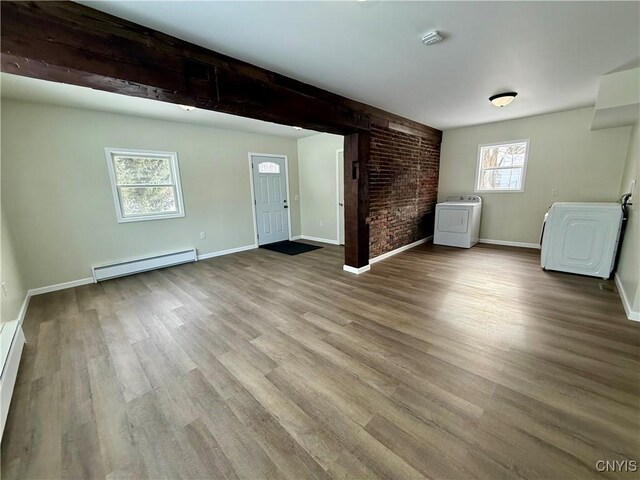 interior space featuring light wood-type flooring, washer / clothes dryer, brick wall, and a baseboard heating unit