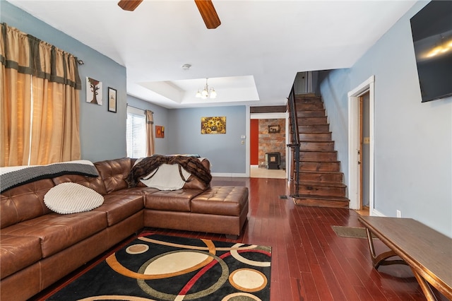 living room featuring ceiling fan with notable chandelier, a fireplace, dark hardwood / wood-style floors, and a tray ceiling