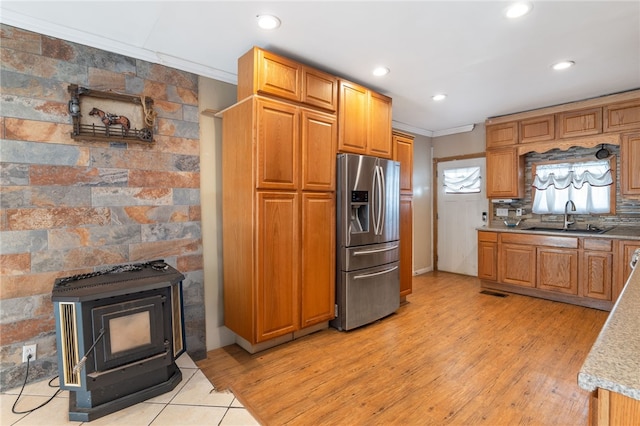 kitchen with crown molding, stainless steel fridge, a wood stove, sink, and backsplash