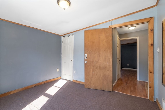 unfurnished bedroom with a closet, crown molding, and dark carpet