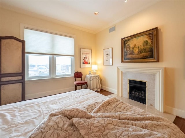 bedroom featuring wood-type flooring, a premium fireplace, and ornamental molding