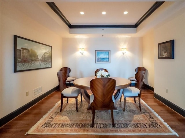 dining space featuring dark hardwood / wood-style flooring, ornamental molding, and a tray ceiling