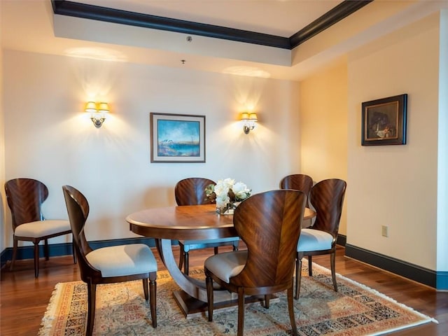 dining space with a tray ceiling, crown molding, and dark wood-type flooring